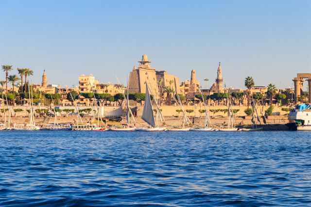 Luxor Temple pylons and palms seen across the Nile with feluccas moored