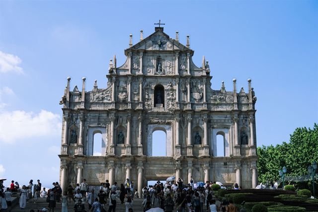 Baroque stone facade of the Ruins of St Paul's in Macau above its crowded stairway under blue sky