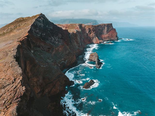 Aerial view of Madeira's rugged red and ochre cliffs and sea stacks in deep blue Atlantic water