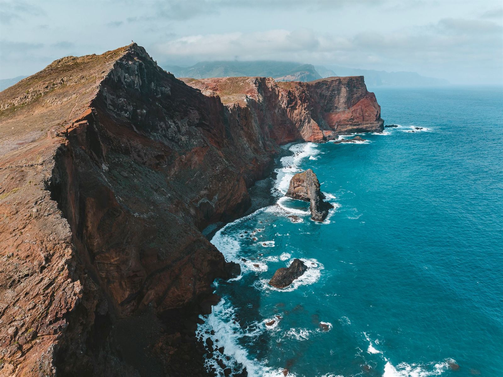 Aerial view of Madeira's rugged red and ochre cliffs and sea stacks in deep blue Atlantic water