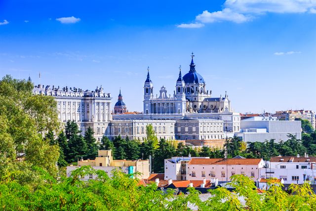 Royal Palace of Madrid and Almudena Cathedral rising above green parkland under blue sky