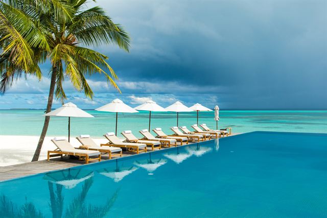 Infinity pool with sunbeds and parasols by the Indian Ocean in South Ari Atoll