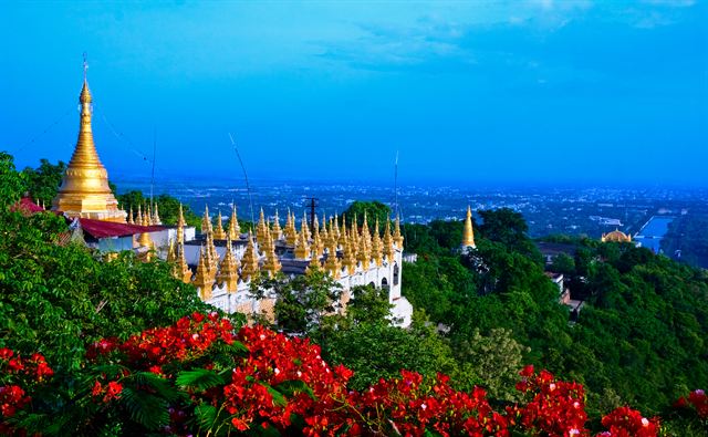 Golden pagoda on Mandalay Hill among trees and red flowers overlooking the plain