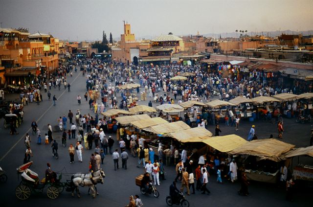 Crowds and market stalls on Jemaa el-Fnaa square in Marrakech with the medina behind, Morocco