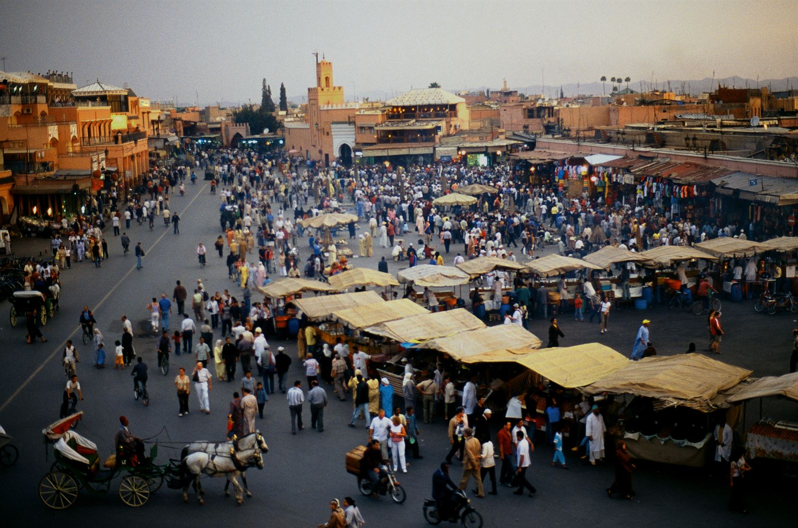 Crowds and market stalls on Jemaa el-Fnaa square in Marrakech with the medina behind, Morocco