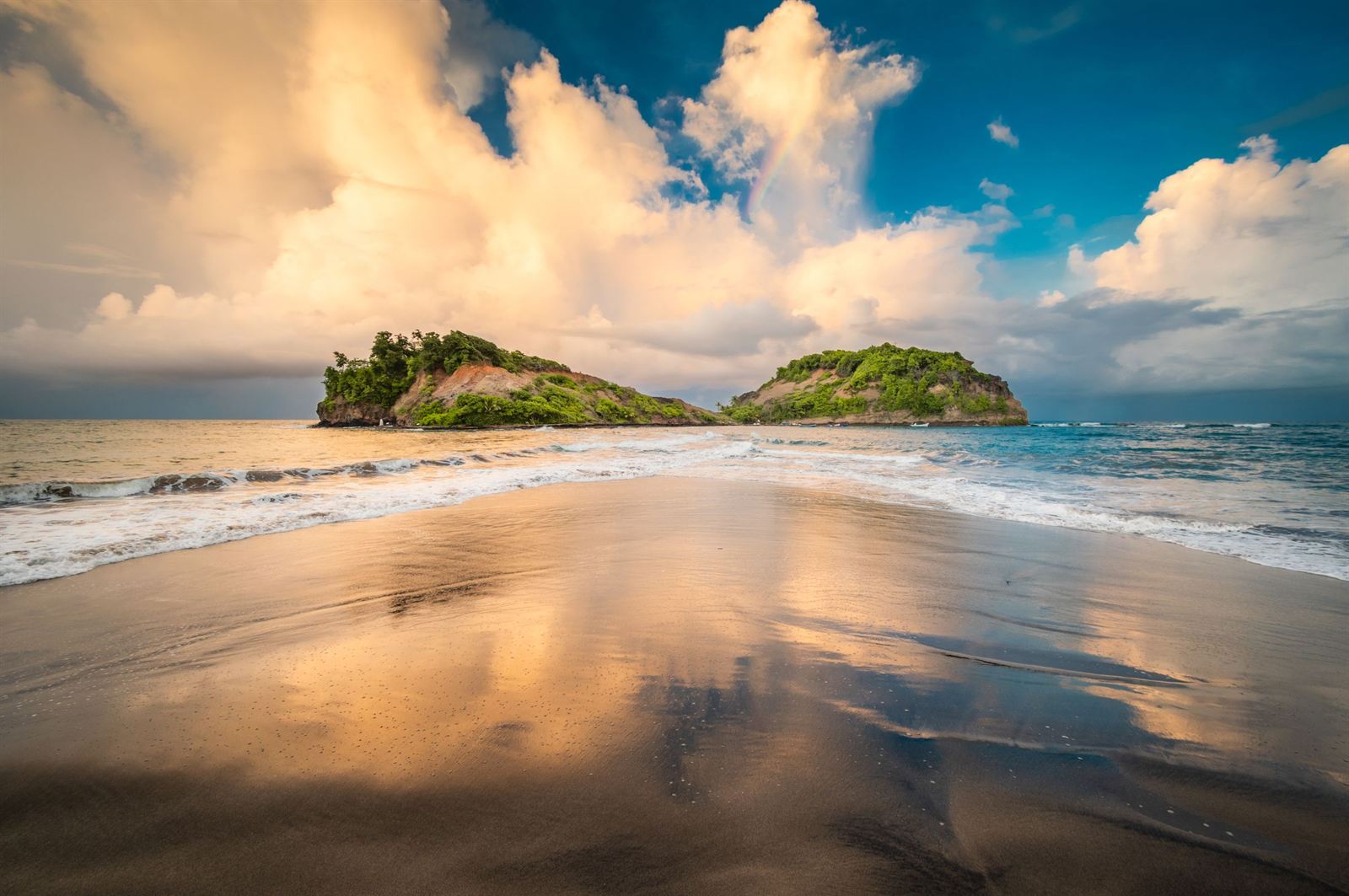 Two small green islets offshore from a wet sandy beach at Sainte-Marie, Martinique, under dramatic clouds