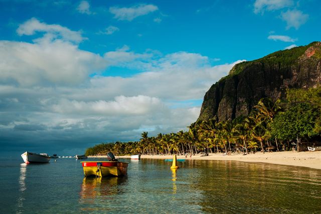 Le Morne Brabant's forested cliff above a palm-lined beach and boats in the Mauritius lagoon