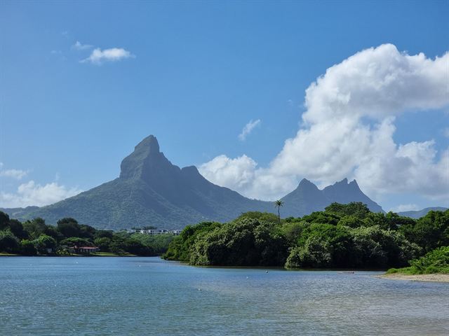 Jagged volcanic peaks of Mauritius rising above green forest and a calm lagoon under blue sky