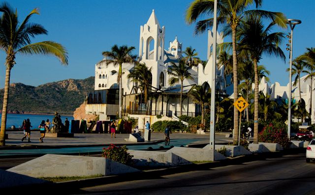 Mazatlan seafront malecon with palm trees and a white seaside building, hills in the background