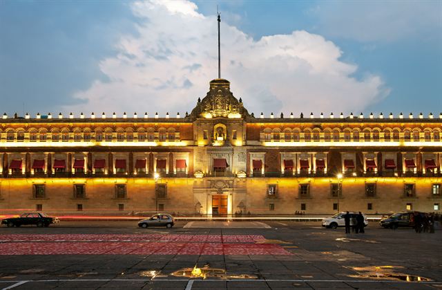 Illuminated National Palace facade on the Zocalo, Mexico City, at dusk with a flagpole