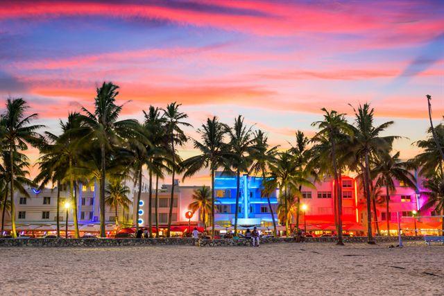 Art Deco hotels on Ocean Drive, Miami Beach, lit in neon at sunset behind palm trees