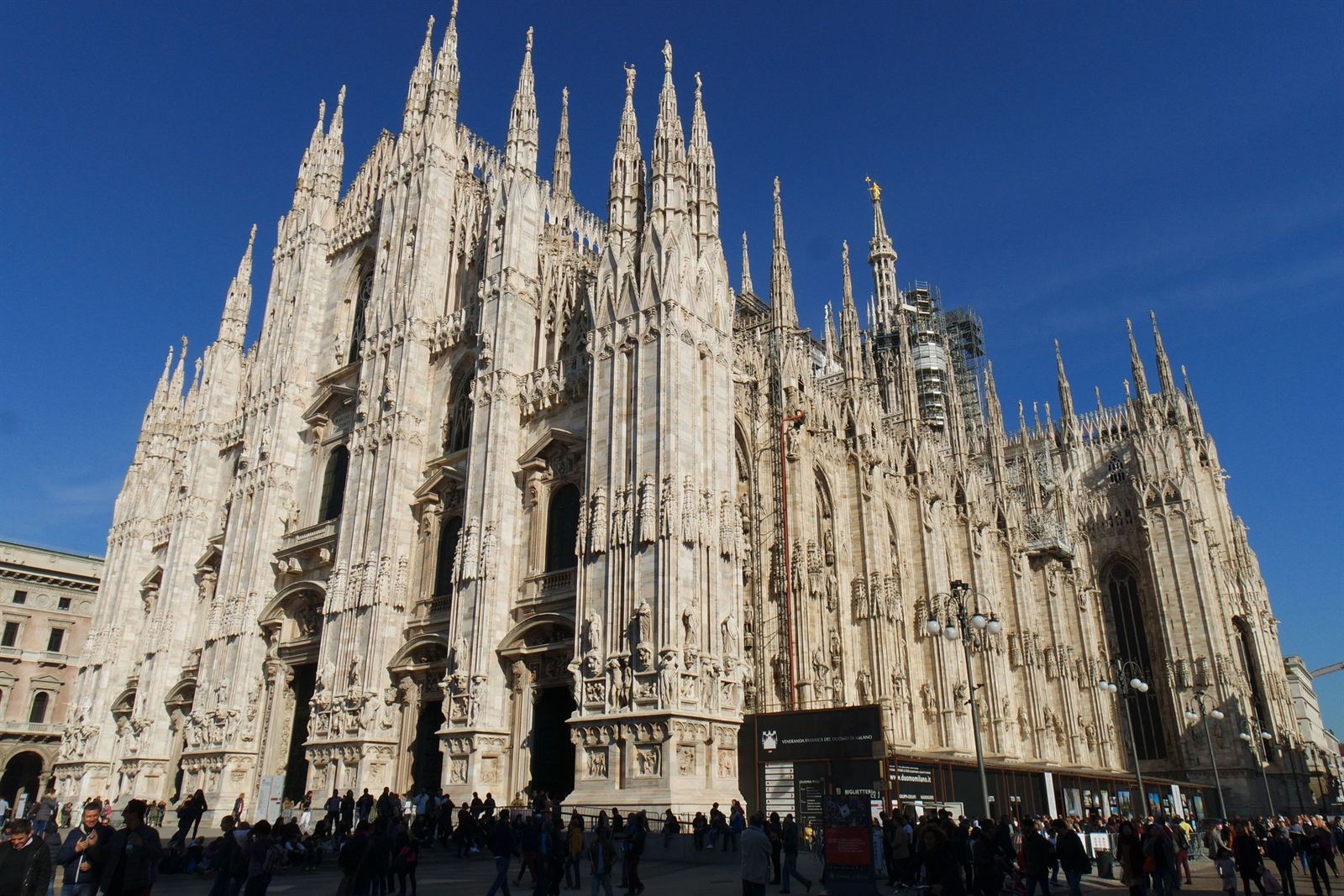 Milan Cathedral (Duomo di Milano) Gothic white marble facade and spires under deep blue sky, crowds in the piazza