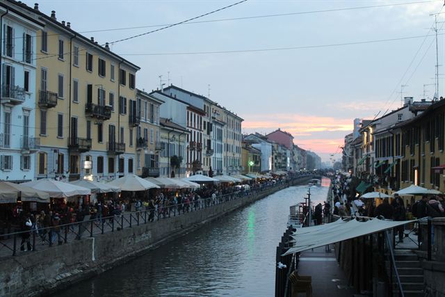 Naviglio Grande canal in Milan at dusk lined with pastel buildings and waterside cafe terraces