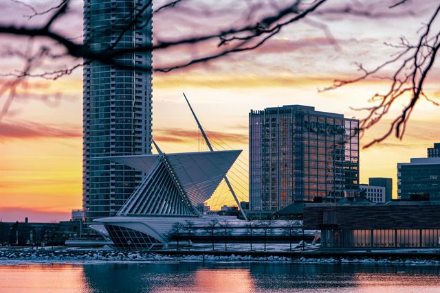 Milwaukee Art Museum's winged Calatrava pavilion and lakefront towers silhouetted against an orange sunset