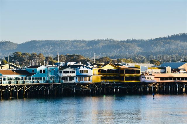 Colorful buildings of Old Fisherman's Wharf in Monterey on pilings over the calm bay with wooded hills behind