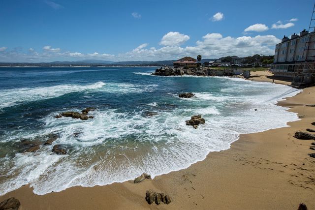 Waves washing onto a curving Monterey beach beside rocky outcrops and waterfront buildings