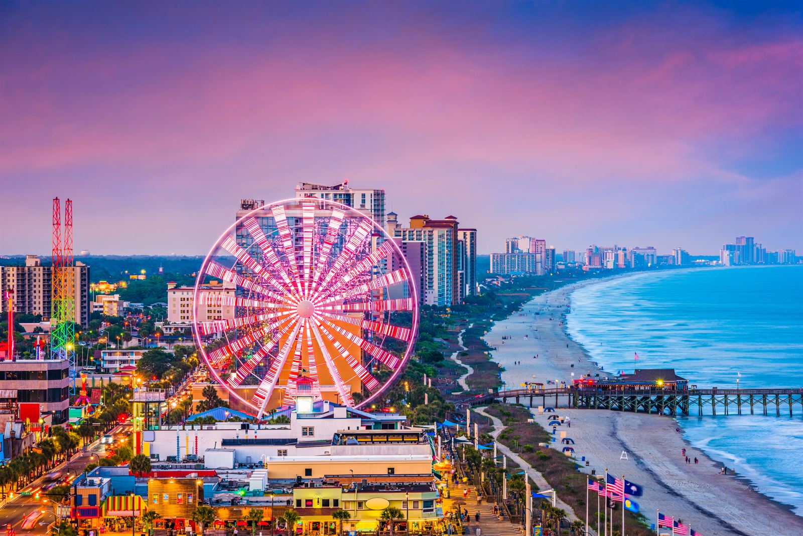 Myrtle Beach SkyWheel lit up beside the boardwalk, pier and oceanfront hotels at pink twilight