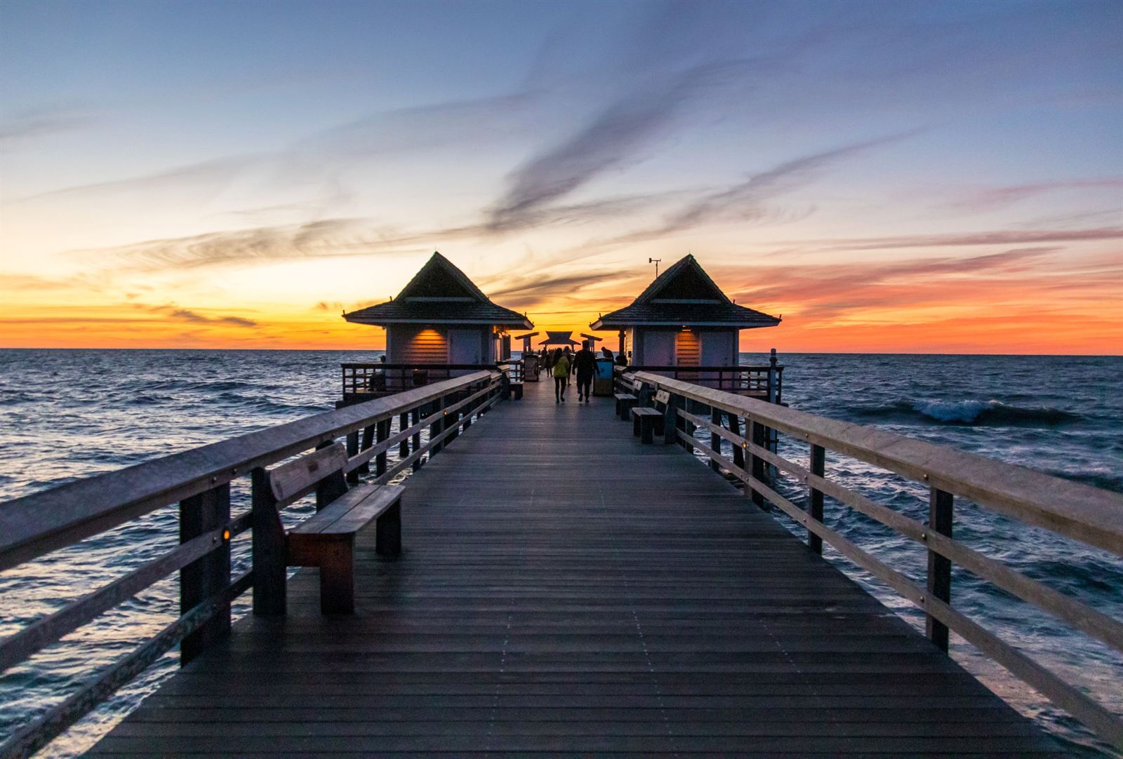 Naples Pier boardwalk leading to its roofed pavilions over the Gulf of Mexico at a colorful sunset