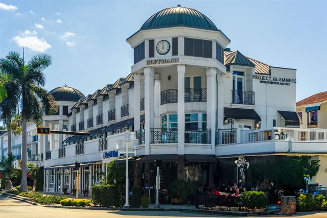 White Mediterranean-style shopping arcade with a domed clock tower and palm trees in Naples, Florida