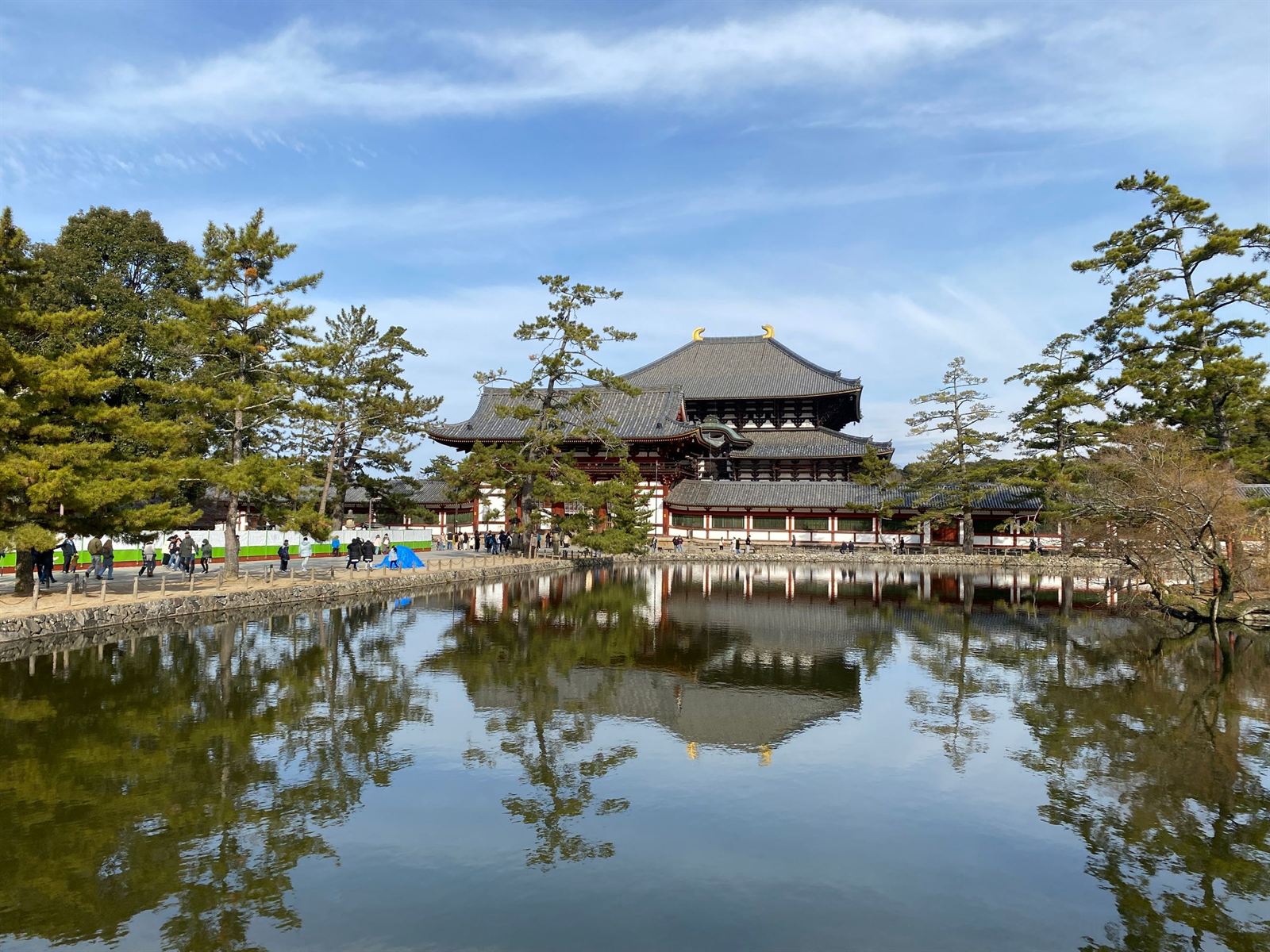 Todai-ji's Great Buddha Hall reflected in a calm pond framed by pine trees in Nara