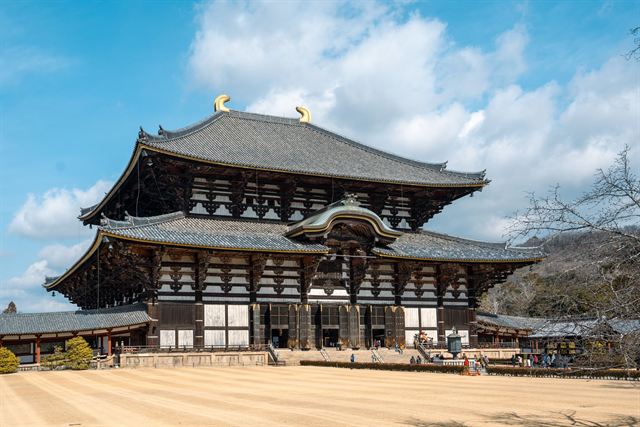 Massive wooden Daibutsuden hall of Todai-ji temple in Nara with golden roof ornaments under blue sky