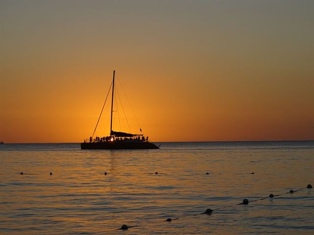 Catamaran silhouetted against an orange sunset over the Caribbean Sea off Negril, Jamaica