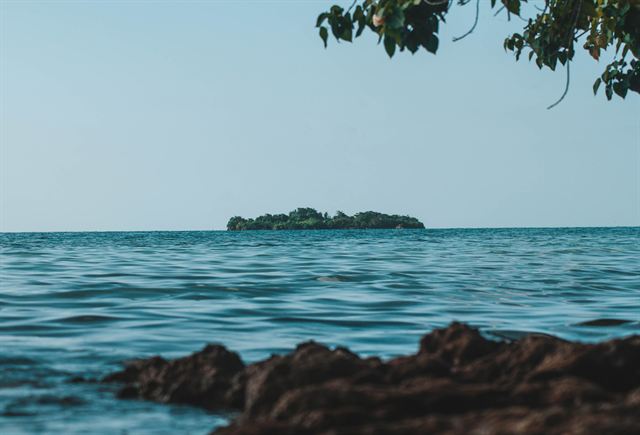 Small forested cay seen across blue water from the rocky Negril shoreline, Jamaica