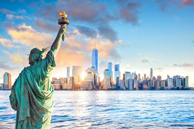 Statue of Liberty in the foreground with the Lower Manhattan skyline and One World Trade Center at sunset