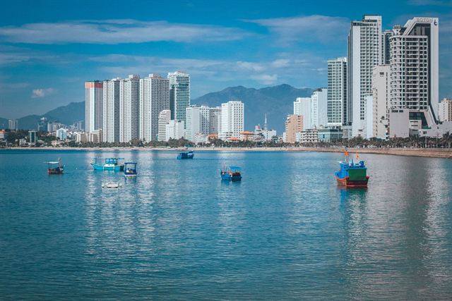 Nha Trang bay with fishing boats on calm blue water in front of beachfront high-rise towers and mountains