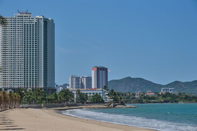 Curving sandy Nha Trang beach with high-rise hotels and green mountains under blue sky
