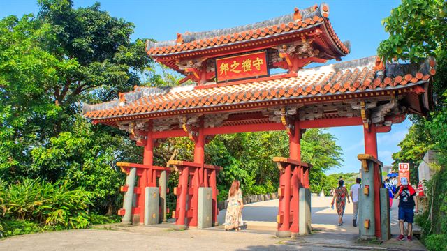 Shureimon, the red-roofed ceremonial gate of Shuri Castle in Okinawa among green trees