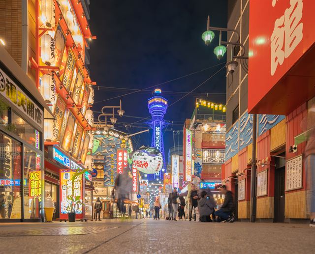 Neon-lit Shinsekai street in Osaka at night with Tsutenkaku Tower at the end