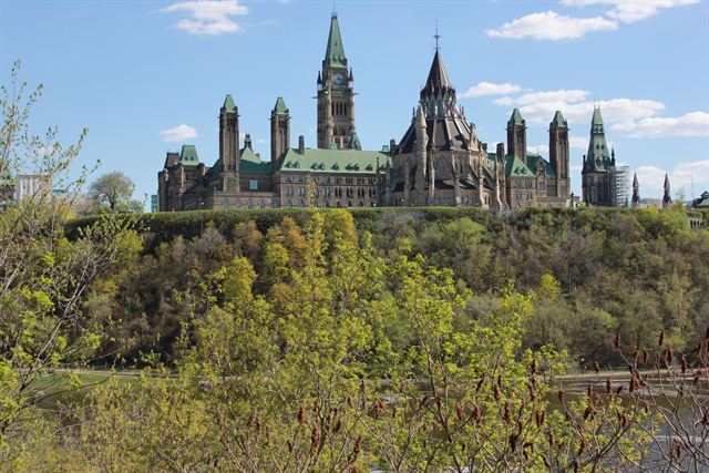 Gothic Revival Parliament buildings and Peace Tower atop Parliament Hill above spring greenery in Ottawa