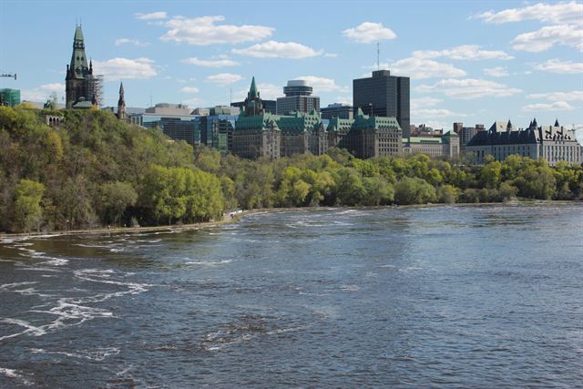 Parliament Hill and downtown Ottawa rising above the tree-lined Ottawa River on a clear day