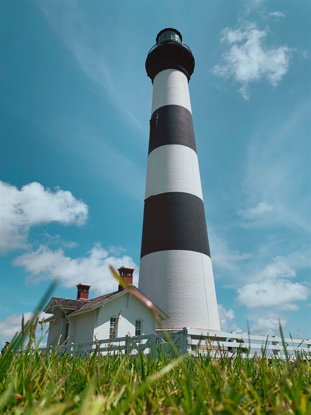Black-and-white striped Bodie Island Lighthouse and keeper's house under blue sky near Nags Head