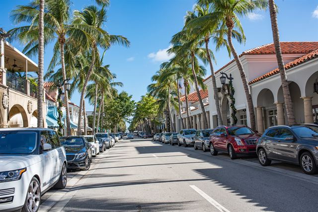 Palm-lined shopping street with Mediterranean-style arcades and parked cars