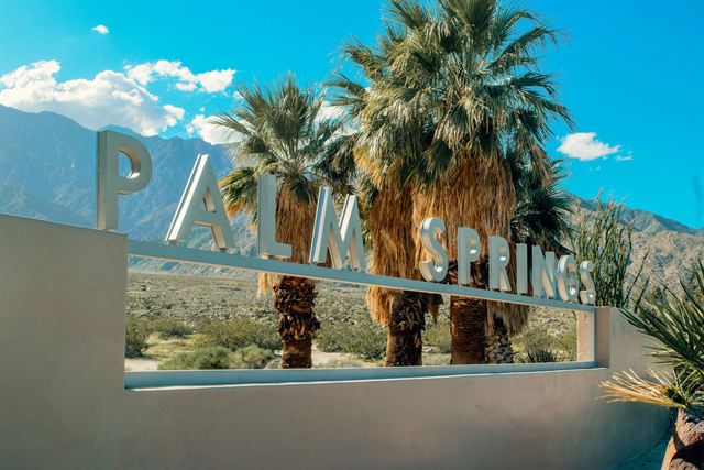 Palm Springs welcome sign lettering with tall fan palms and desert mountains under a blue sky