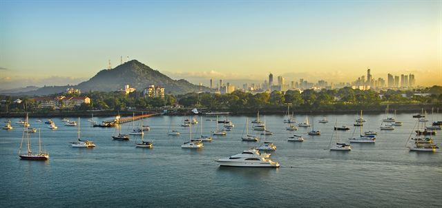 Panama City skyline and Cerro Ancon behind a bay full of moored sailboats at sunrise