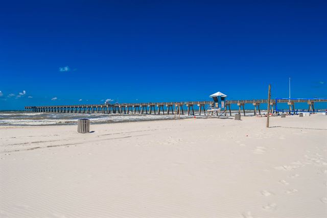 White sand beach at Panama City Beach with a long fishing pier and lifeguard stand under deep blue sky