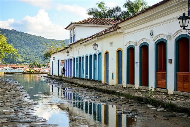 Whitewashed colonial houses with colored doors reflected in a flooded cobblestone street in Paraty