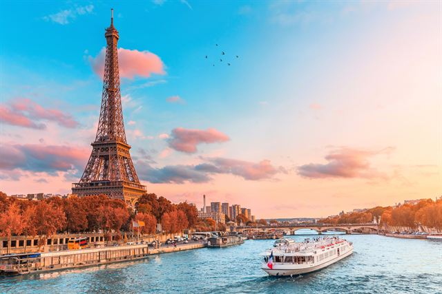 Eiffel Tower at sunset with autumn trees and a river cruise boat on the Seine