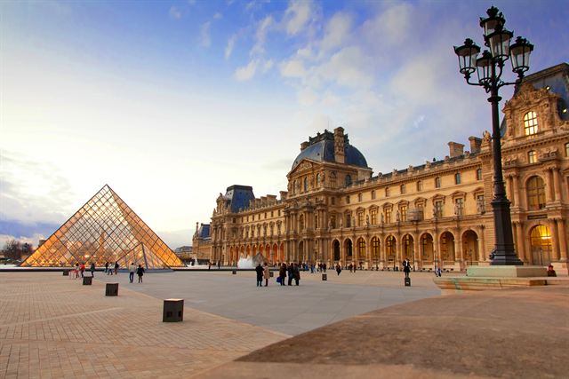 The Louvre glass pyramid and palace courtyard under a blue sky