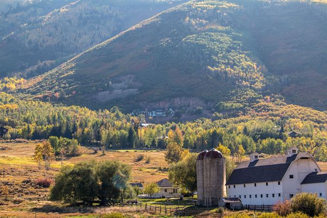 The white McPolin Barn and silo in Park City, Utah beneath mountainsides in golden autumn color