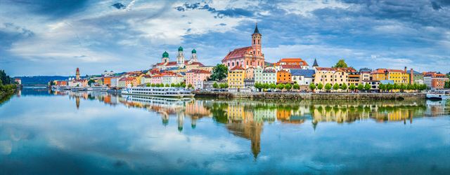 Panorama of Passau riverfront with church towers reflected in calm water
