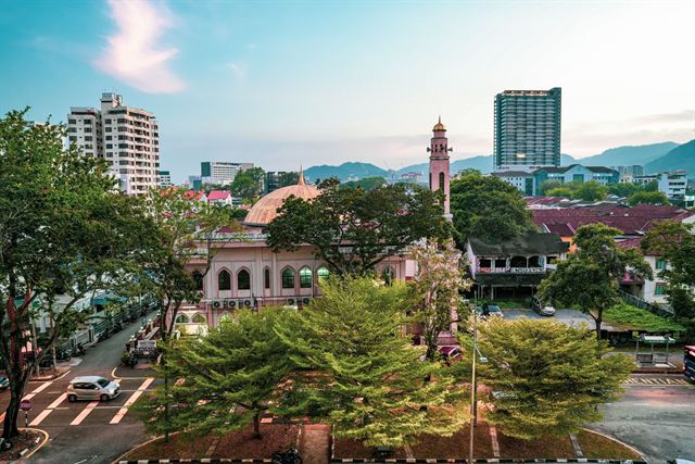 Kapitan Keling Mosque's domes and minaret among trees and high-rises in George Town, Penang