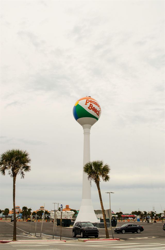 The iconic Pensacola Beach Ball water tower rising above palm trees under a cloudy sky