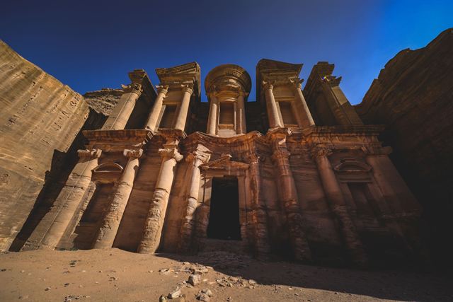 The Monastery (Ad Deir) facade carved into a sandstone cliff at Petra under a deep blue sky