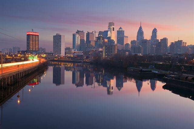 Philadelphia skyline at dusk reflected in the Schuylkill River with light trails along the riverside expressway
