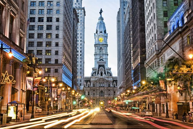 Philadelphia City Hall tower topped by the William Penn statue at the end of a busy Broad Street at night