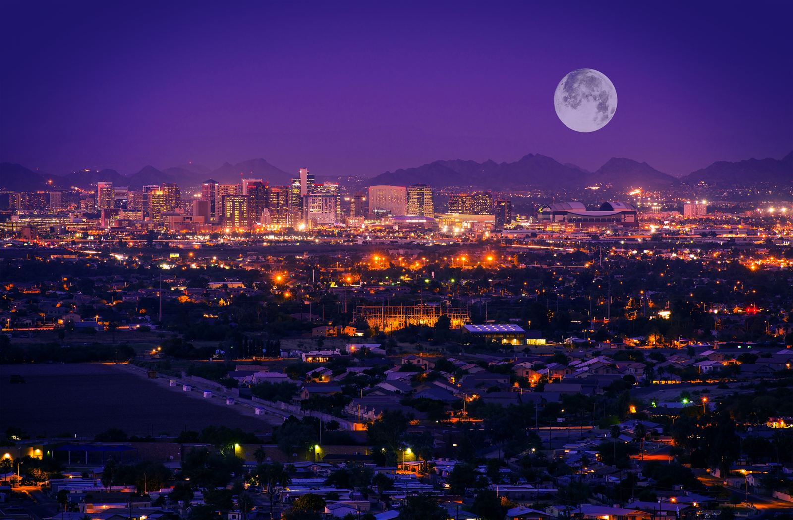 Phoenix city lights at night under a full moon with desert mountains on the horizon, Arizona